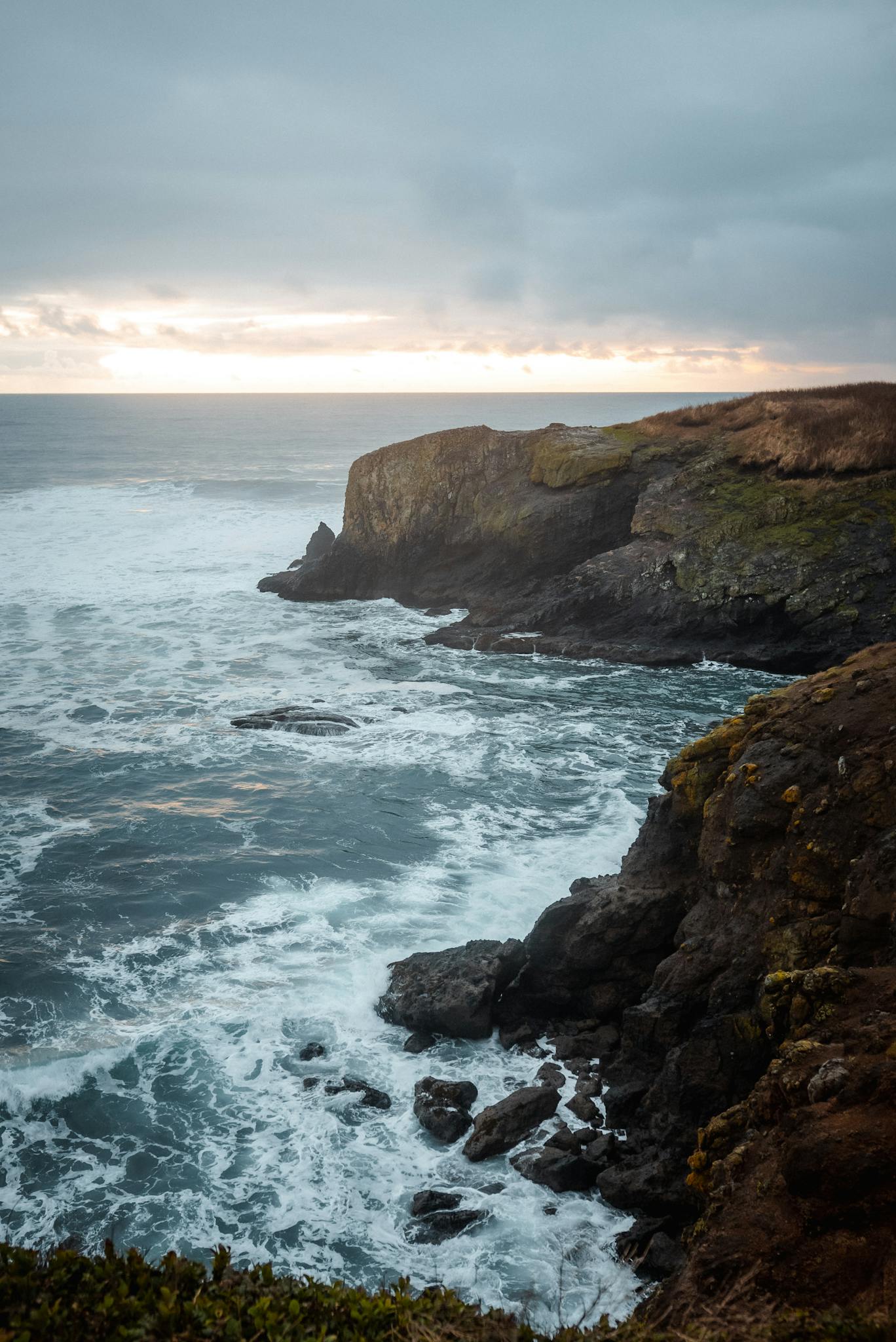 Dramatic coastal cliffs with crashing waves during sunset in Newport, Oregon, USA.