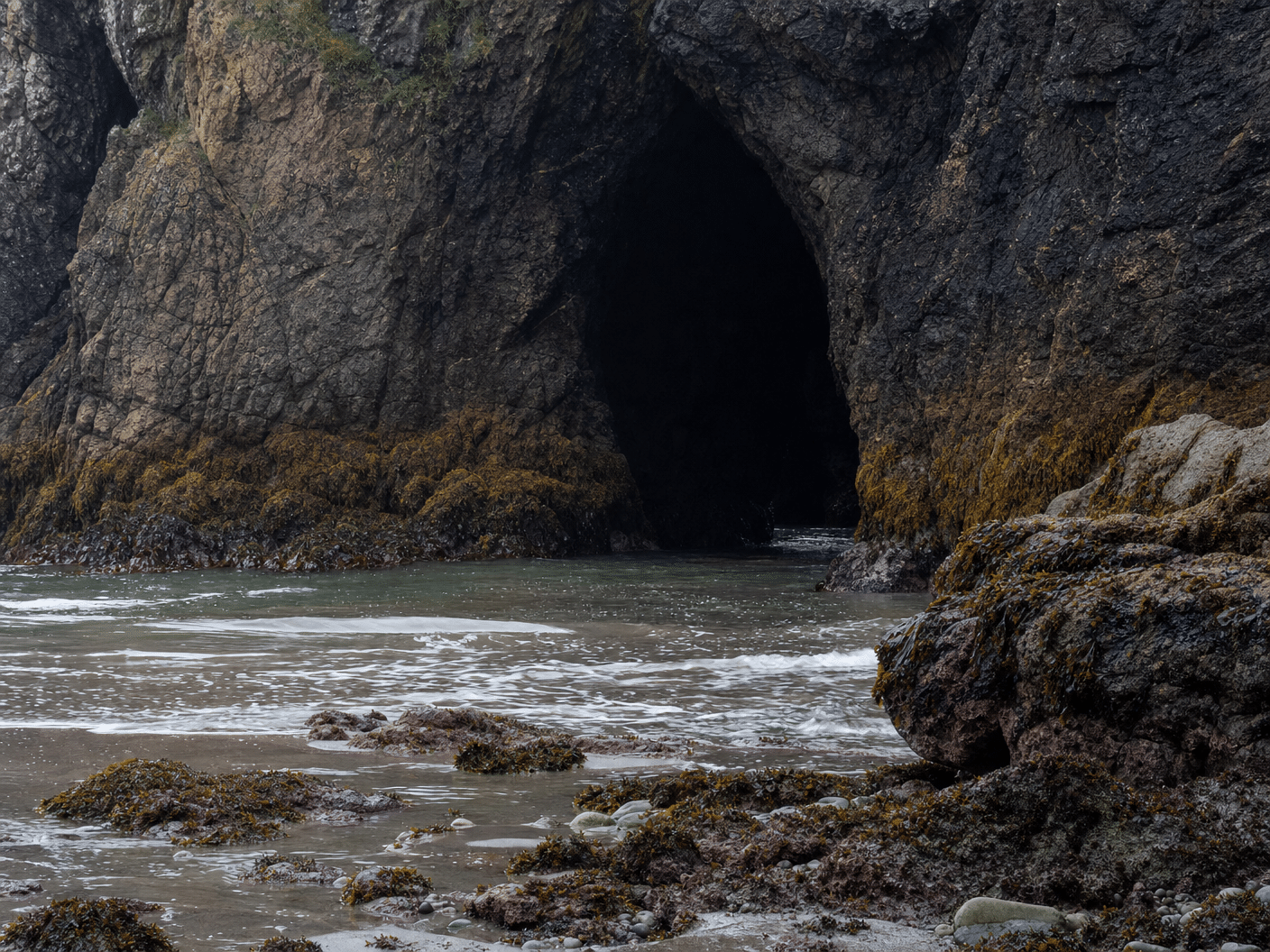 Sea cave entrance in cliff face accessible during low tide on Oregon Coast
