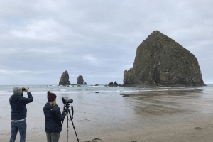 Two visitors using binoculars and a spotting scope near Haystack Rock at Cannon Beach.