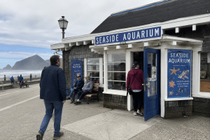 Visitors entering the historic Seaside Aquarium building beside the Oregon Coast promenade.