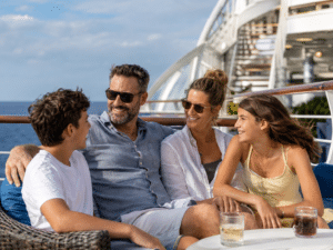 Parents and two teenagers smiling and spending time together on an outdoor cruise ship deck.
