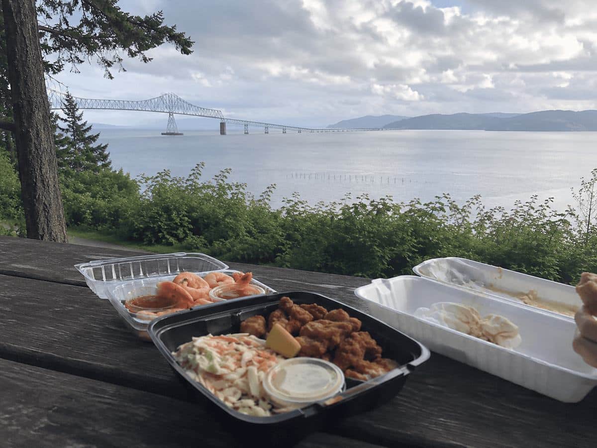 Takeout shrimp, popcorn shrimp, and coleslaw on a picnic table overlooking the Astoria-Megler Bridge and the Columbia River