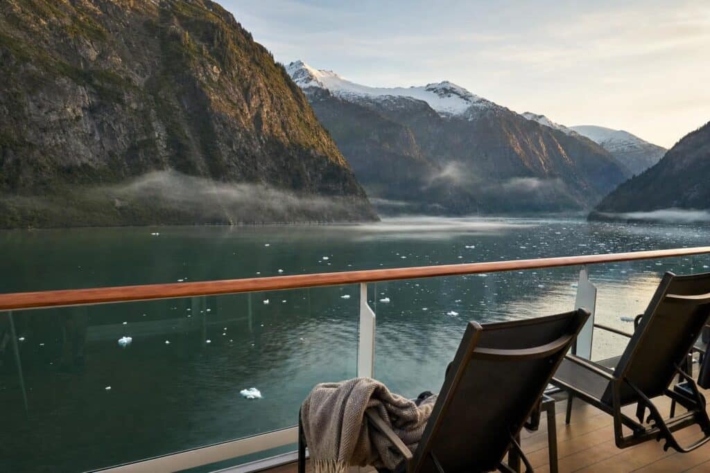 Cruise balcony with two deck chairs overlooking a misty Alaska fjord and snowy mountains at sunrise