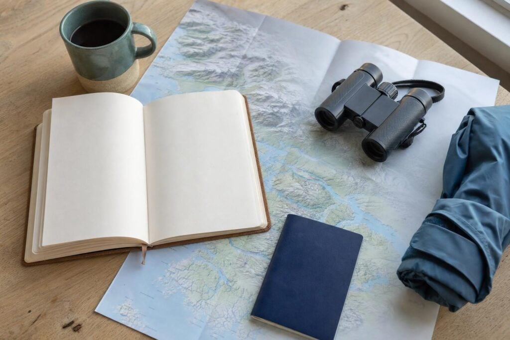 Flat-lay of passport, binoculars, map and notebook for planning a 7-night Alaska Inside Passage cruise