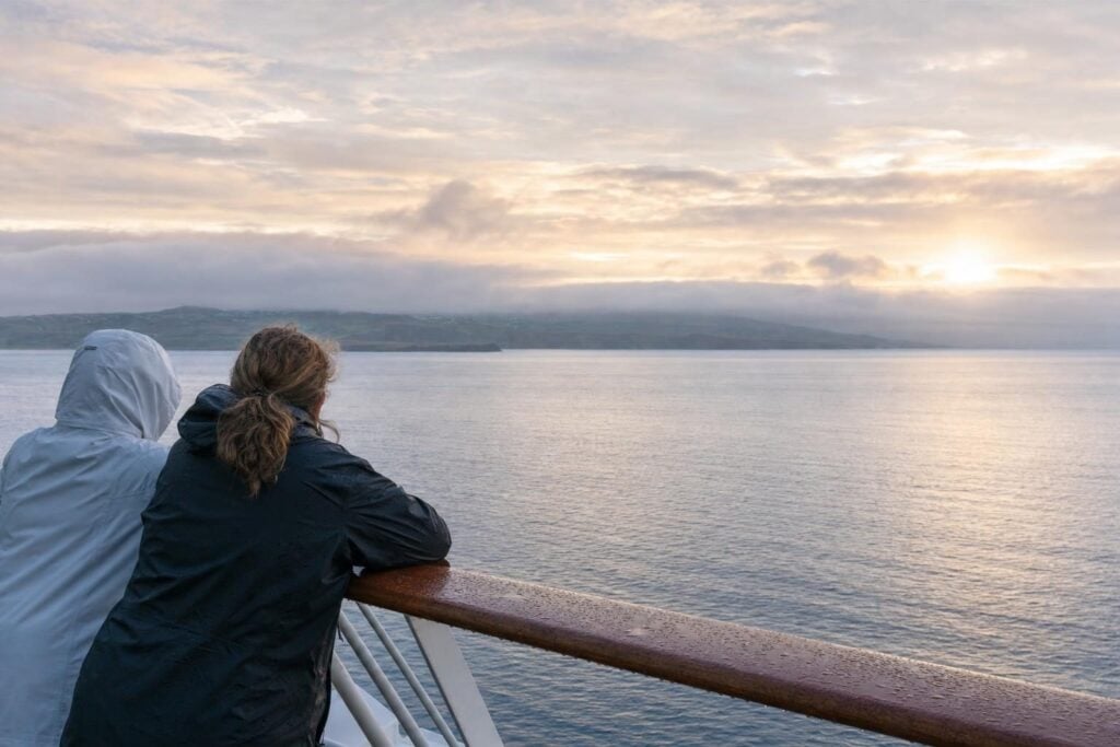 Two passengers at a ship railing at dawn watching the Pacific on a northbound Alaska cruise