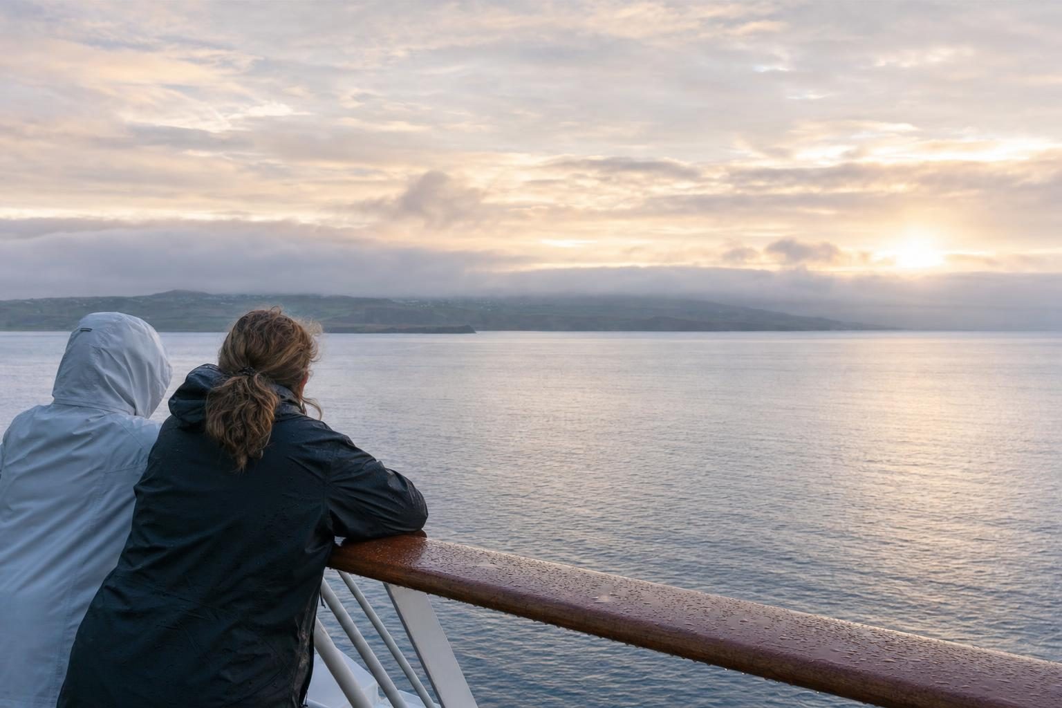 Two passengers at a ship railing at dawn watching the Pacific on a northbound Alaska cruise