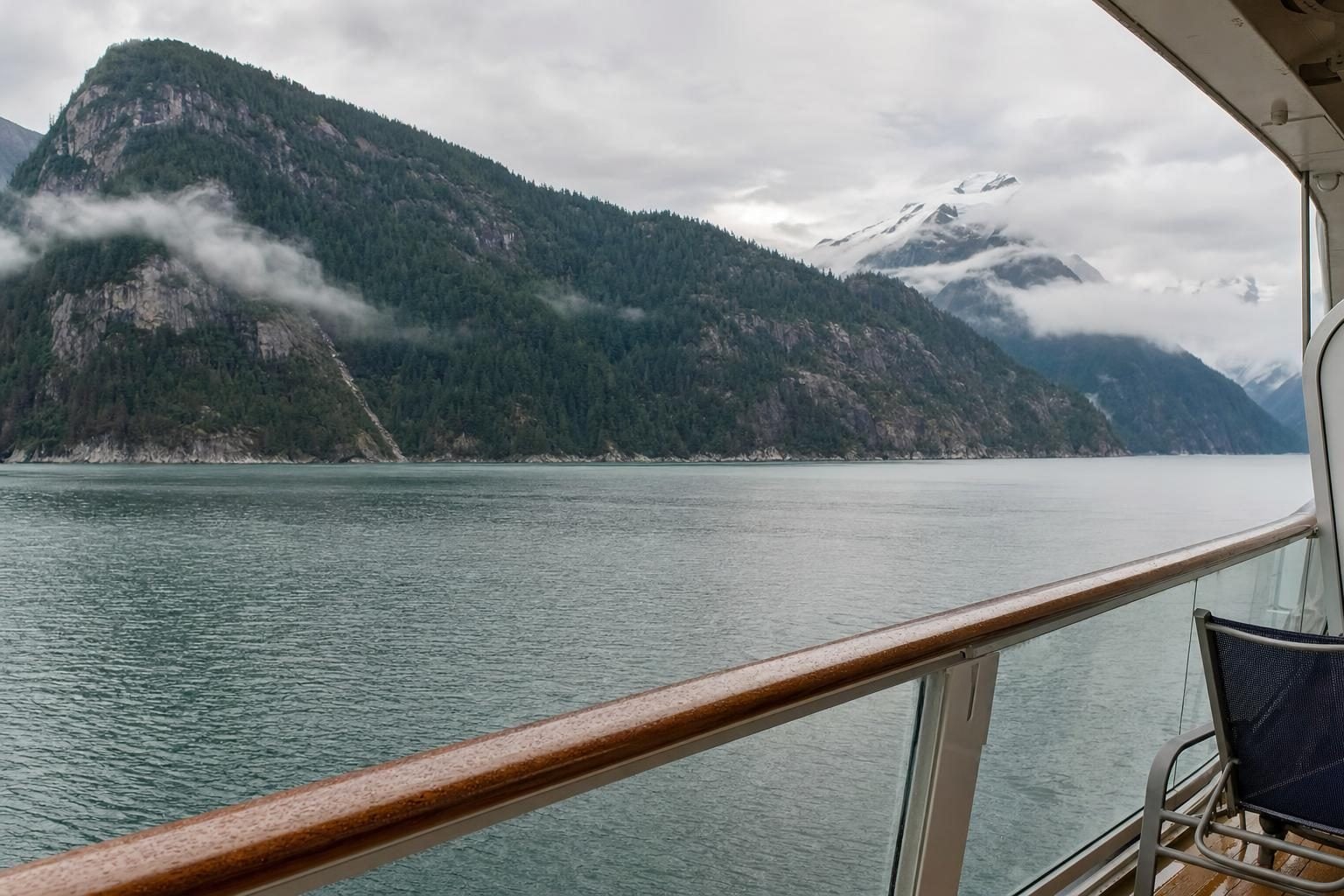 Cruise ship balcony view of misty forested mountains along the Alaska Inside Passage at sunrise