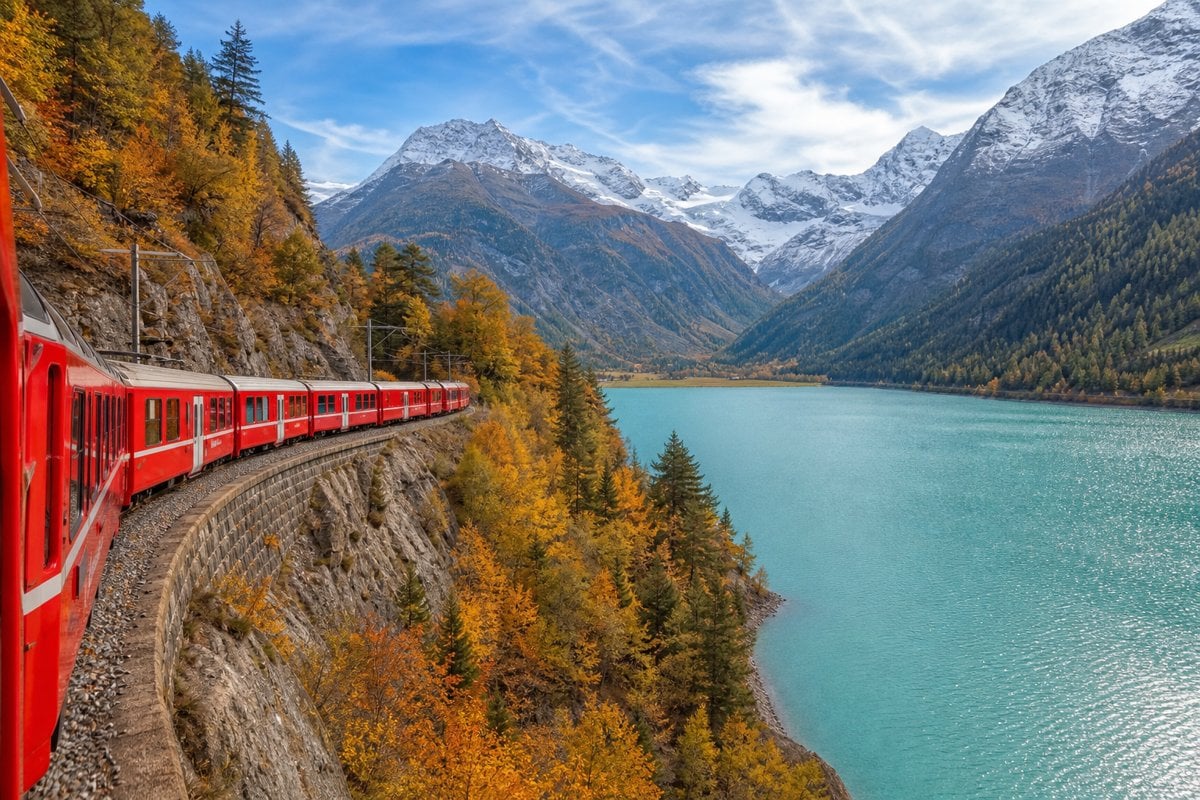 Red train along a mountain lake in the Alps