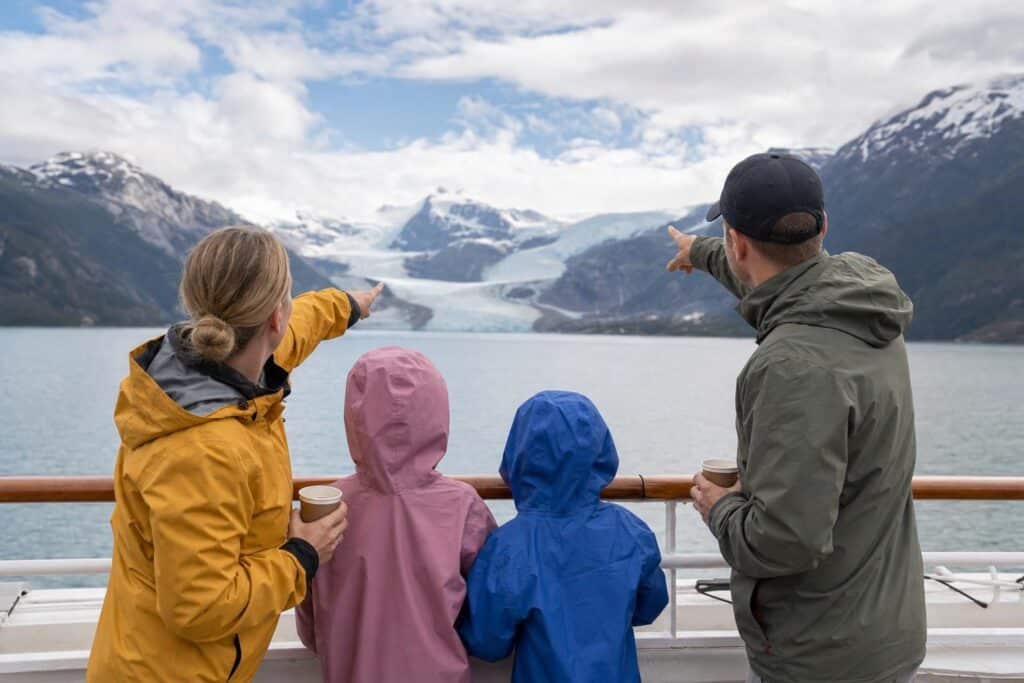 Family in rain jackets on a cruise ship deck looking at a distant glacier on an Alaska sailing