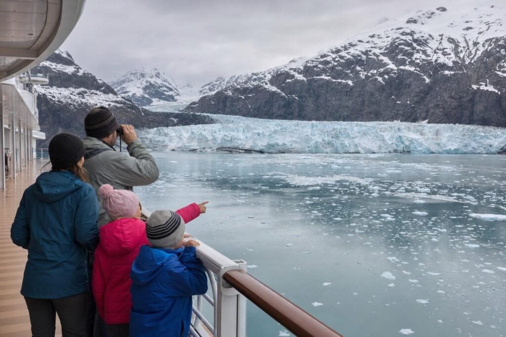Family in rain jackets watching a tidewater glacier from a cruise ship deck in Alaska
