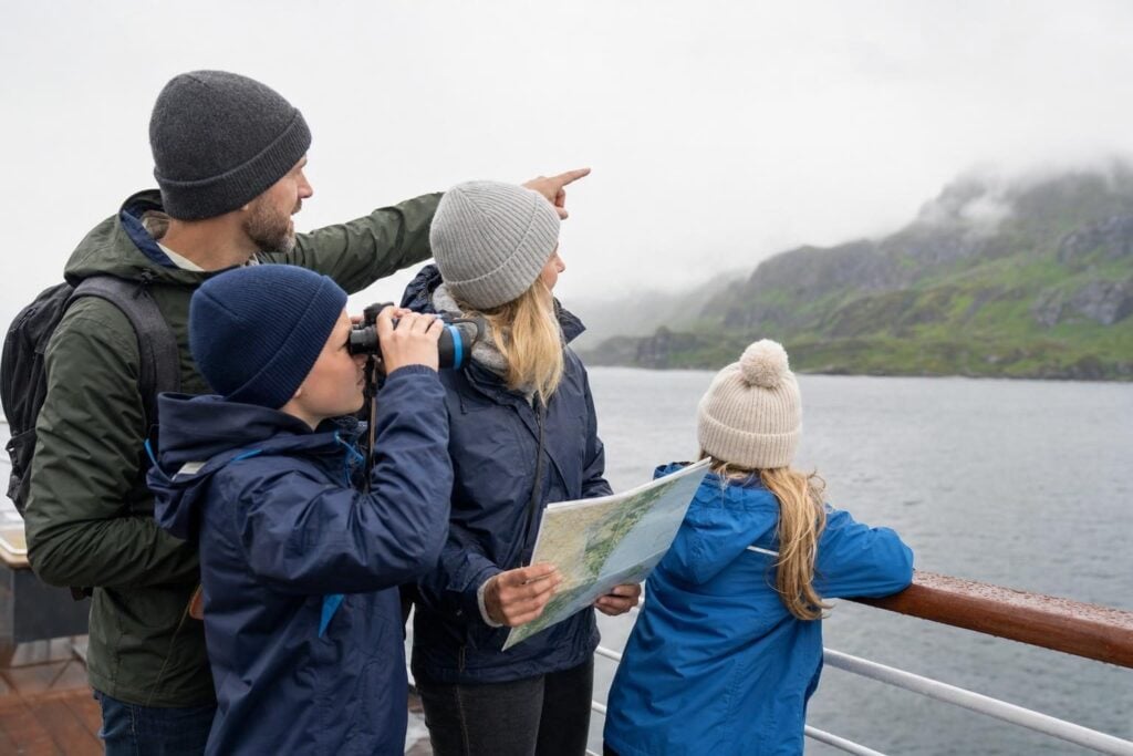 Family in rain jackets on a ship deck watching the Alaska coastline during a 7-day Inside Passage cruise