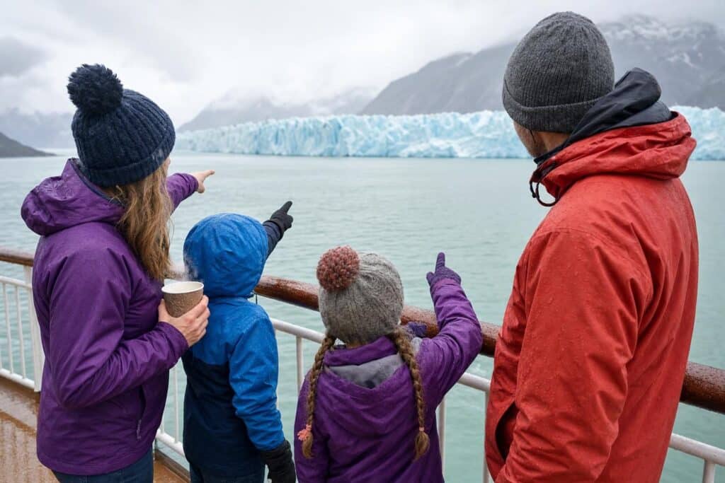 Family in rain jackets on a ship deck watching a glacier on an Alaska cruise