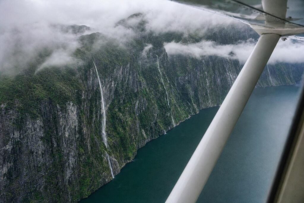 Floatplane view over a steep-walled fjord with waterfalls and dense rainforest in Southeast Alaska