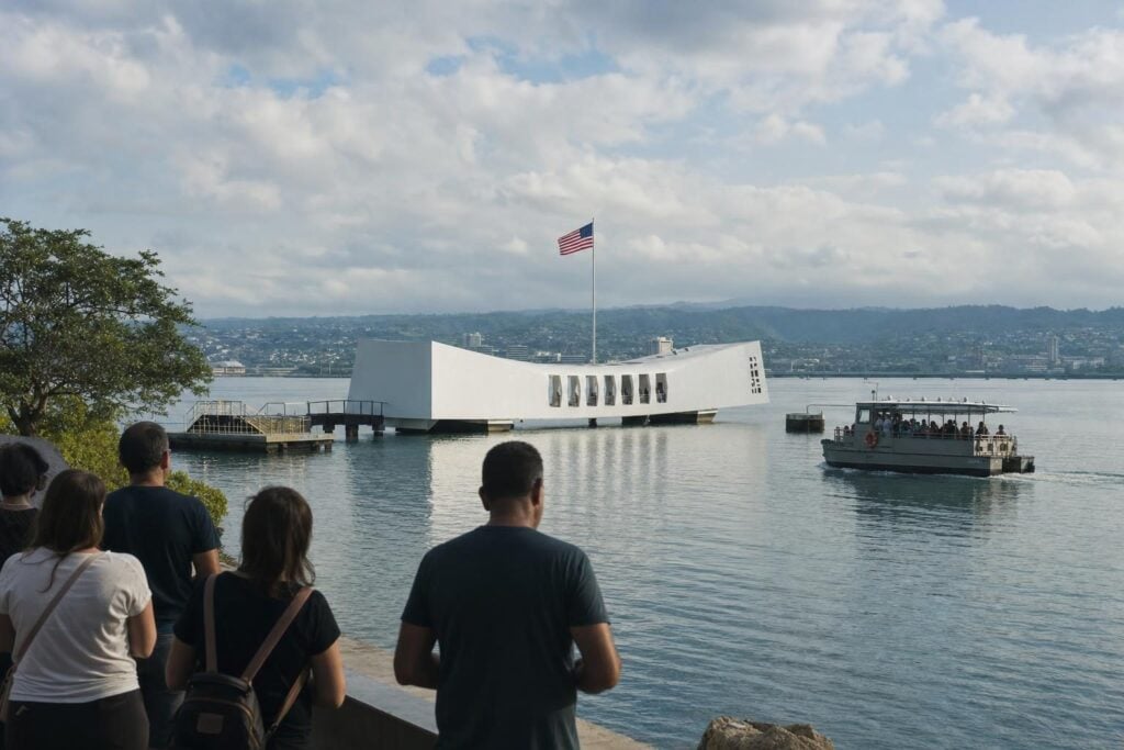 Visitors on a harbor walkway looking toward a white memorial on calm water at Pearl Harbor