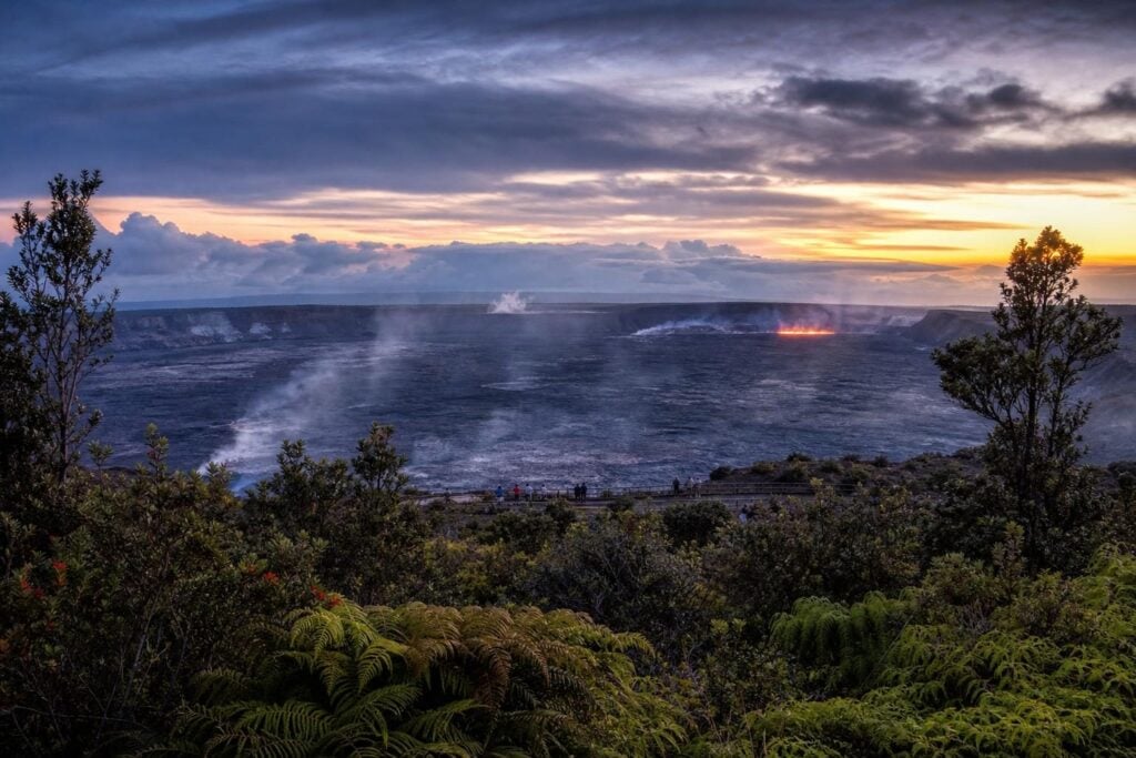 Steaming volcanic crater at dusk with a faint glow, seen from a safe overlook on the Big Island